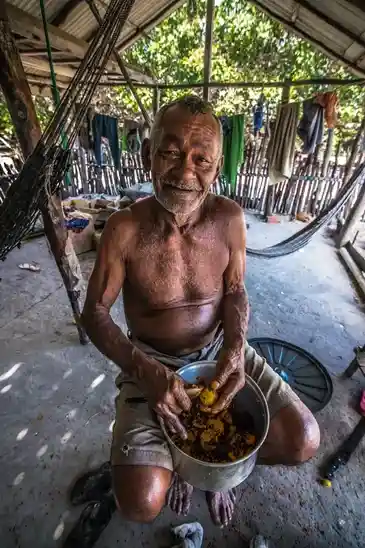 Homem descascando pequi em uma cabana no mato em fotografia autoral de Calblima